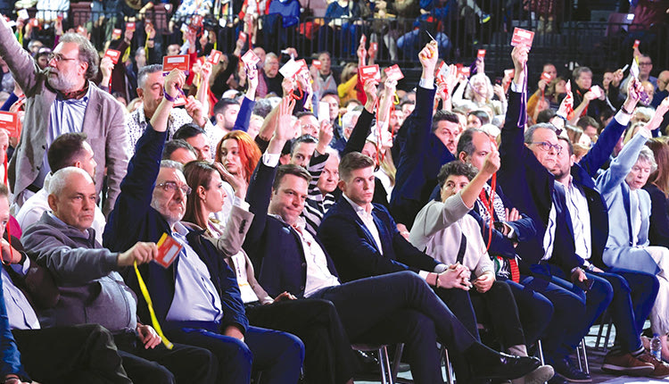 Ήταν όντως ενα από τα παράδοξα του συνεδρίου του κόμματος της αξιωματικής αντιπολίτευσης. Αναφέρομαι στις φωτογραφίες από το Τάε Κβον Ντο, με τον Στέφανο Κασσελάκη να σηκώνει το χέρι του την ώρα της ψηφοφορίας της πρότασης των τριών. Από τη μία, δημοσιεύματα ήθελαν τον πρόεδρο του κόμματος να υπερψηφίζει την πρόταση και κατ’επέκταση να καταψηφίζει τον ίδιο του τον εαυτό που είχε ζητήσει νέα προσφυγή στις εσωκομματικές κάλπες, «σηκώνοντας το γάντι» που του είχε πετάξει ο προκάτοχός του στην ηγεσία. Έτσι, τα στιγμιότυπα με τον πρόεδρο του ΣΥΡΙΖΑ να σηκώνει το χέρι του στην επίμαχη ψηφοφορία δεν θα μπορούσαν να περάσουν απαρατήρητα, με μερίδα του Τύπου να σημειώνει πως στην πραγματικότητα και ο ίδιος ήθελε να αποφύγει τη νέα αναμέτρηση.